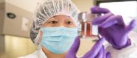 researcher with mask and gloves on holds a container of cells